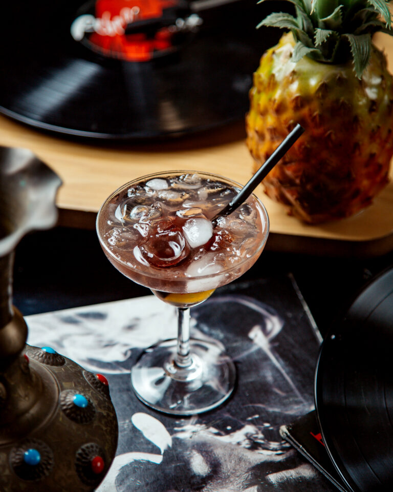 a glass of cocktail with ice cubes and black straw pipe